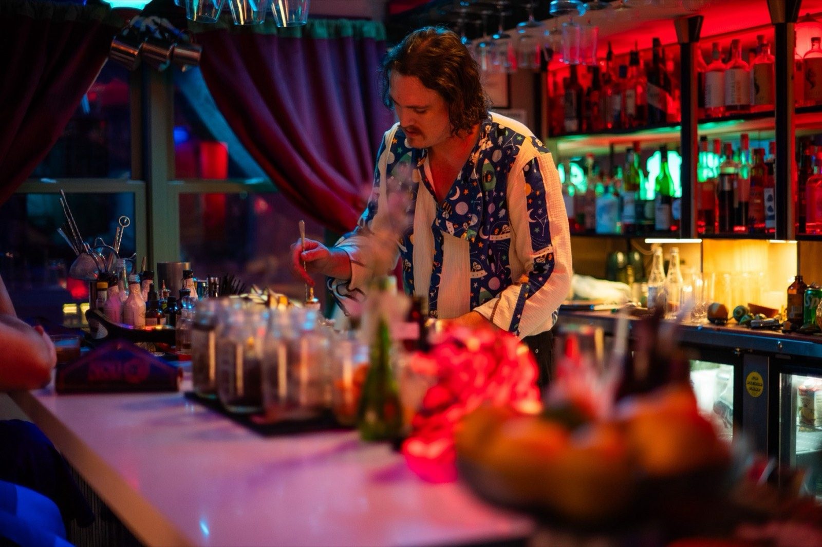 A bartender mixing drinks behind a bar laid with glassware and garnishes