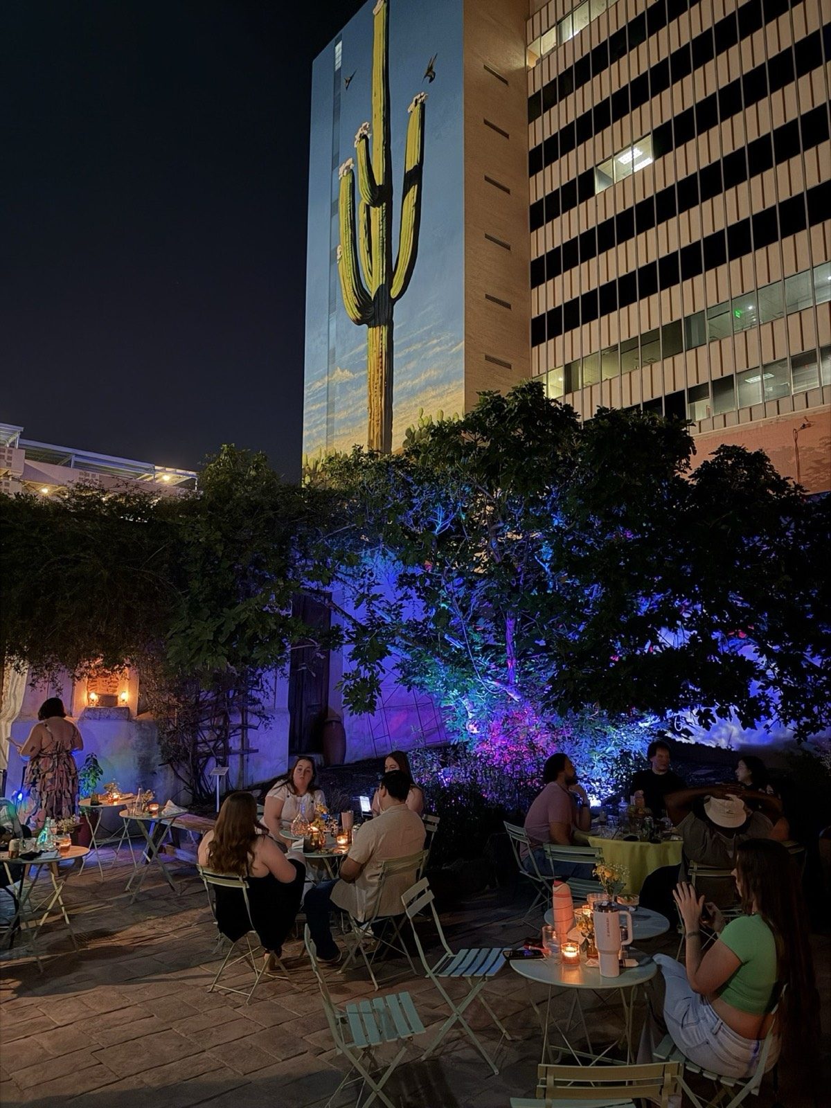 Candlelit tables set beneath string lights and the saguaro mural in the Presidio courtyard