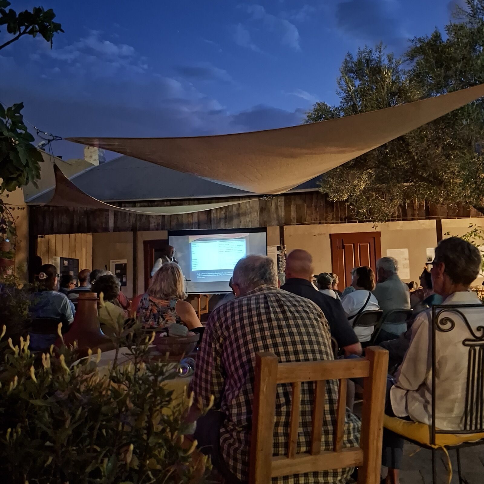 A full audience under the shade sail for an evening presentation on the patio