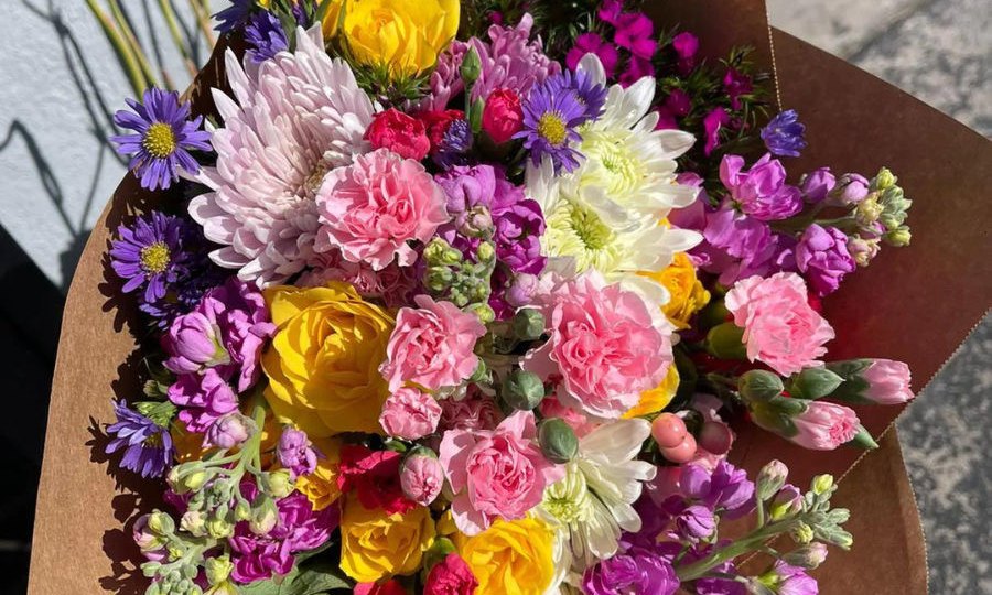 A kraft-wrapped bouquet of pink carnations, yellow roses and purple stock