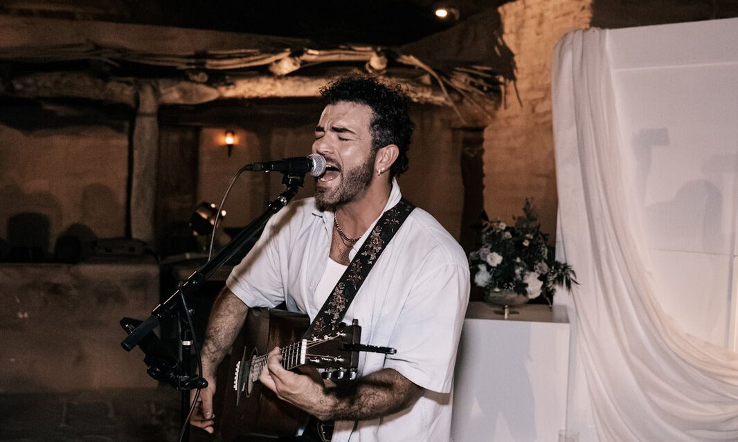 Erick Grillo singing with an acoustic guitar in the courtyard at night