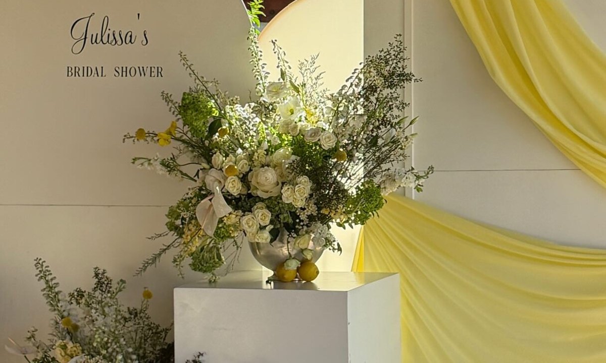 A bridal shower backdrop with white arches, yellow draping and white florals with lemons