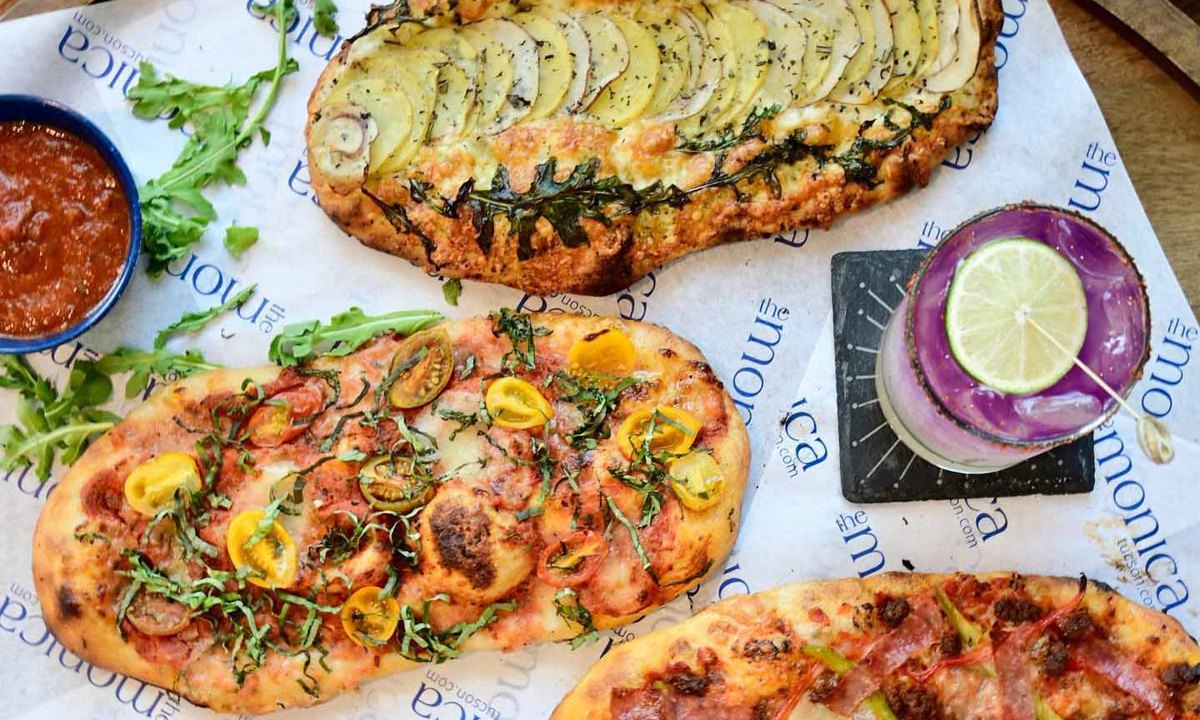 Three flatbread pizzas and a lime-garnished purple cocktail at The Monica